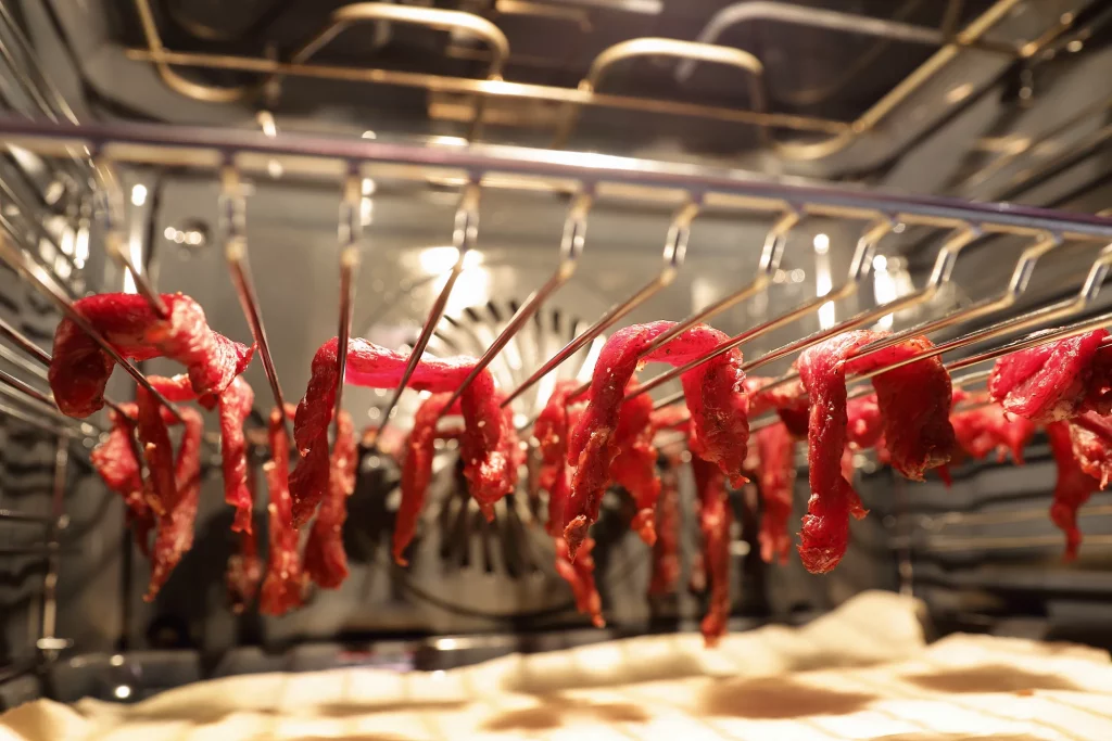 Raw meat hanging over an oven rack to start the beef jerky drying process. 